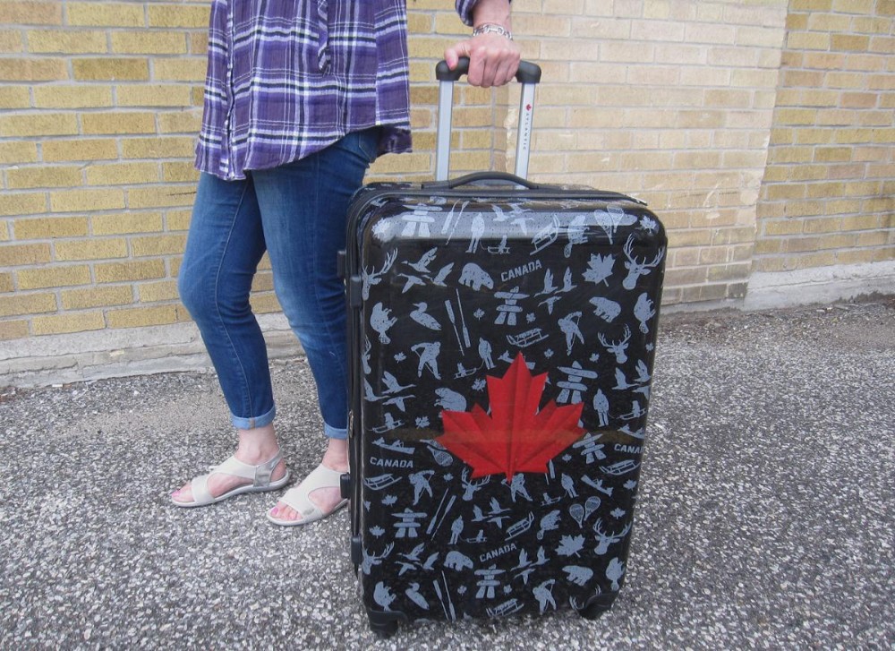 a woman with a suitcase bearing the Canadian maple leaf