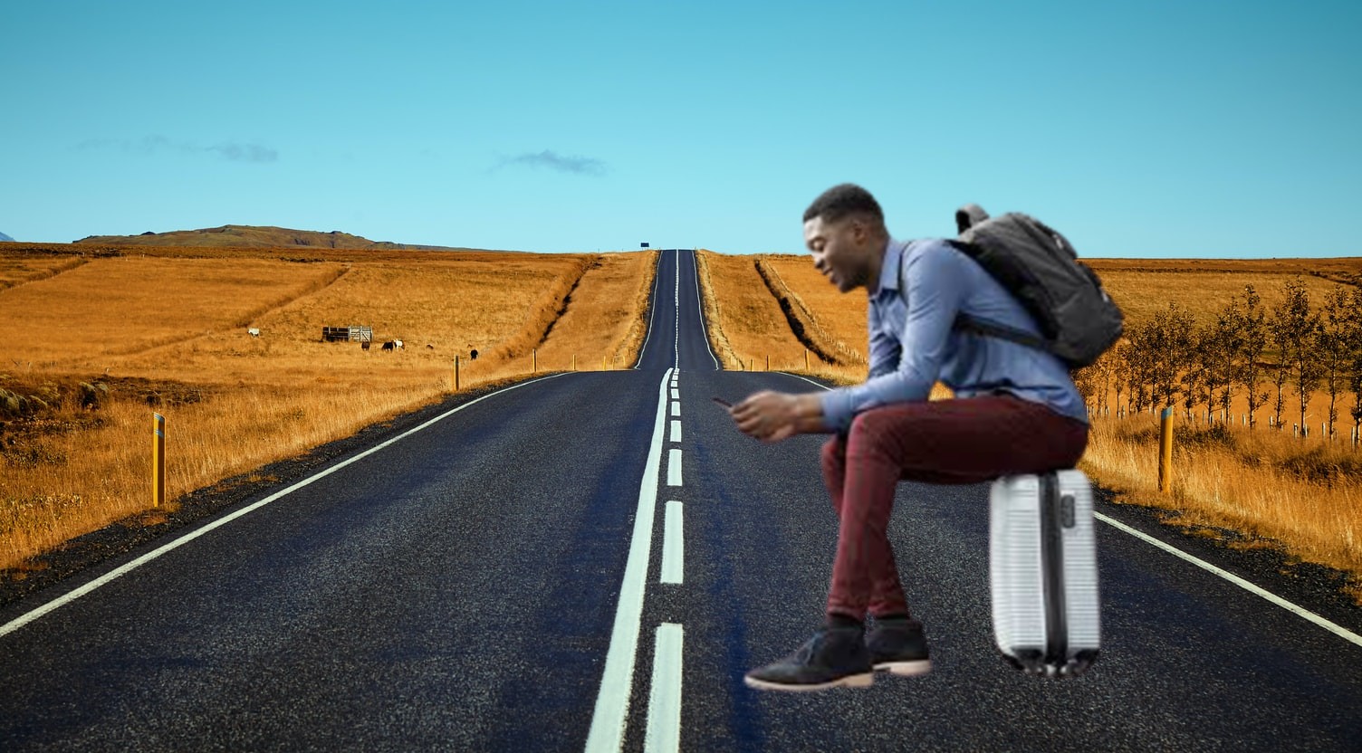 business traveler watching his smartphone and sitting on a suitcase down a long road