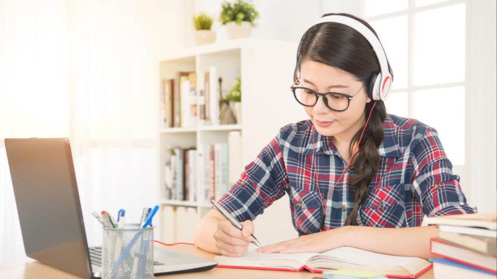 a woman wearing glassing and headphones studies on a laptop